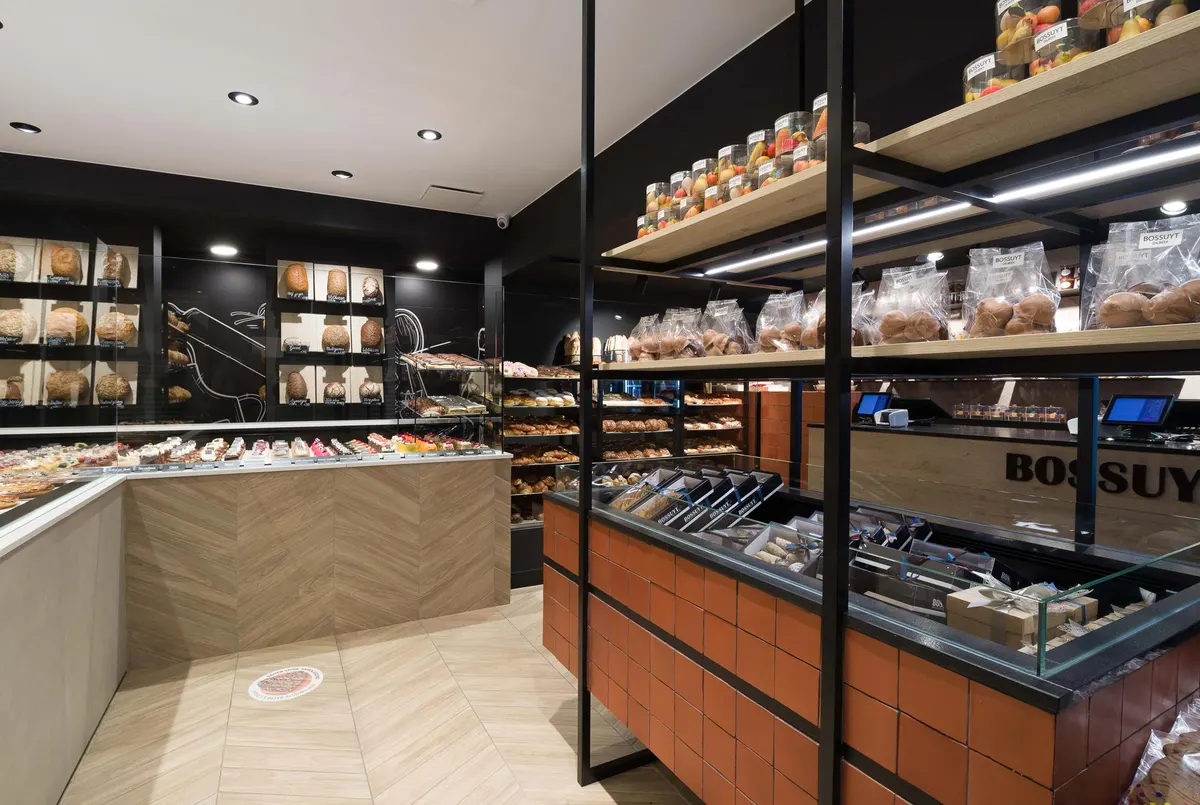 Het interieur van de bakkerij met zwarte wanden, houten rekken en een toonbank met het opschrift Bossuyt